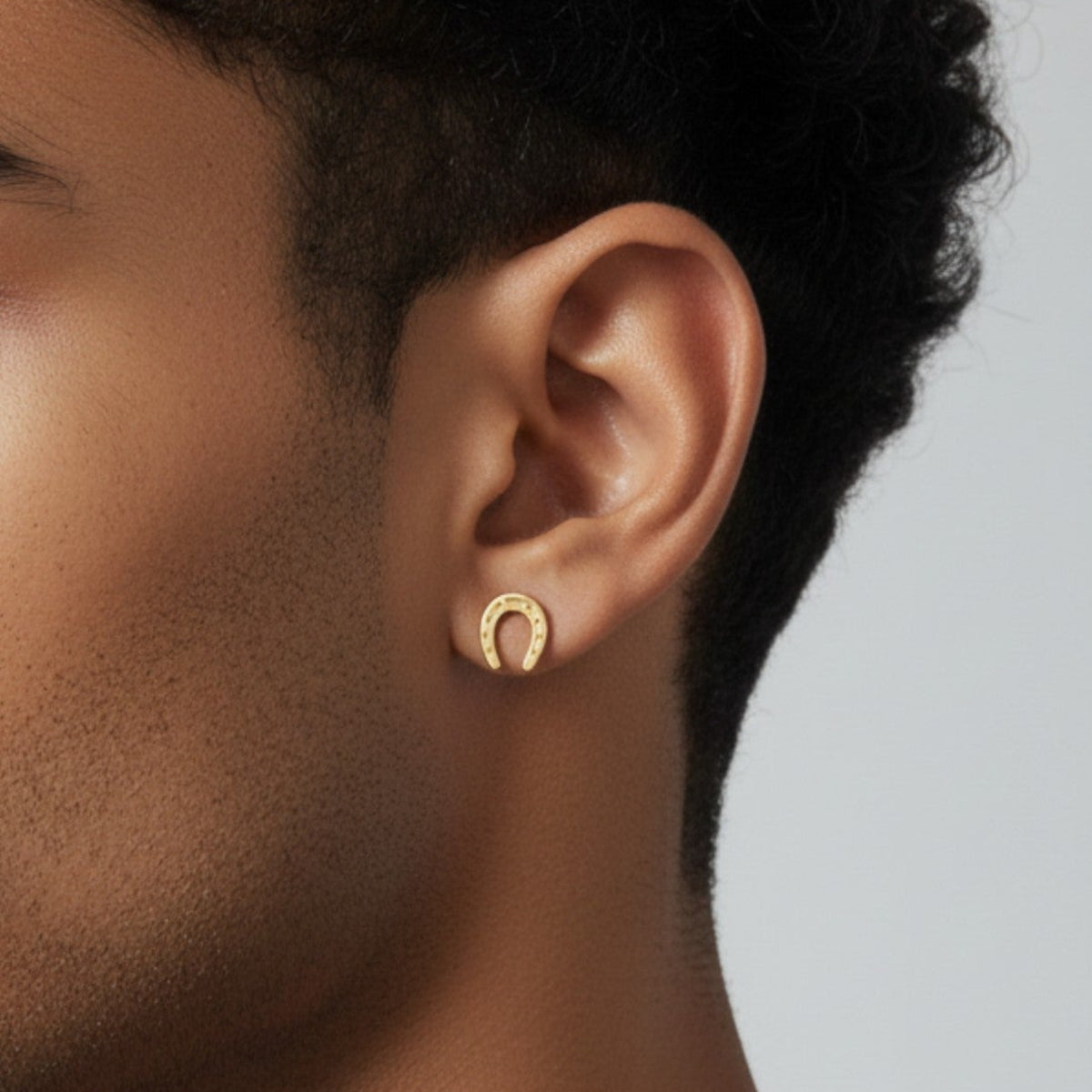 Truelements Jewelry 18k yellow gold horseshoe stud earring worn on a man's earlobe