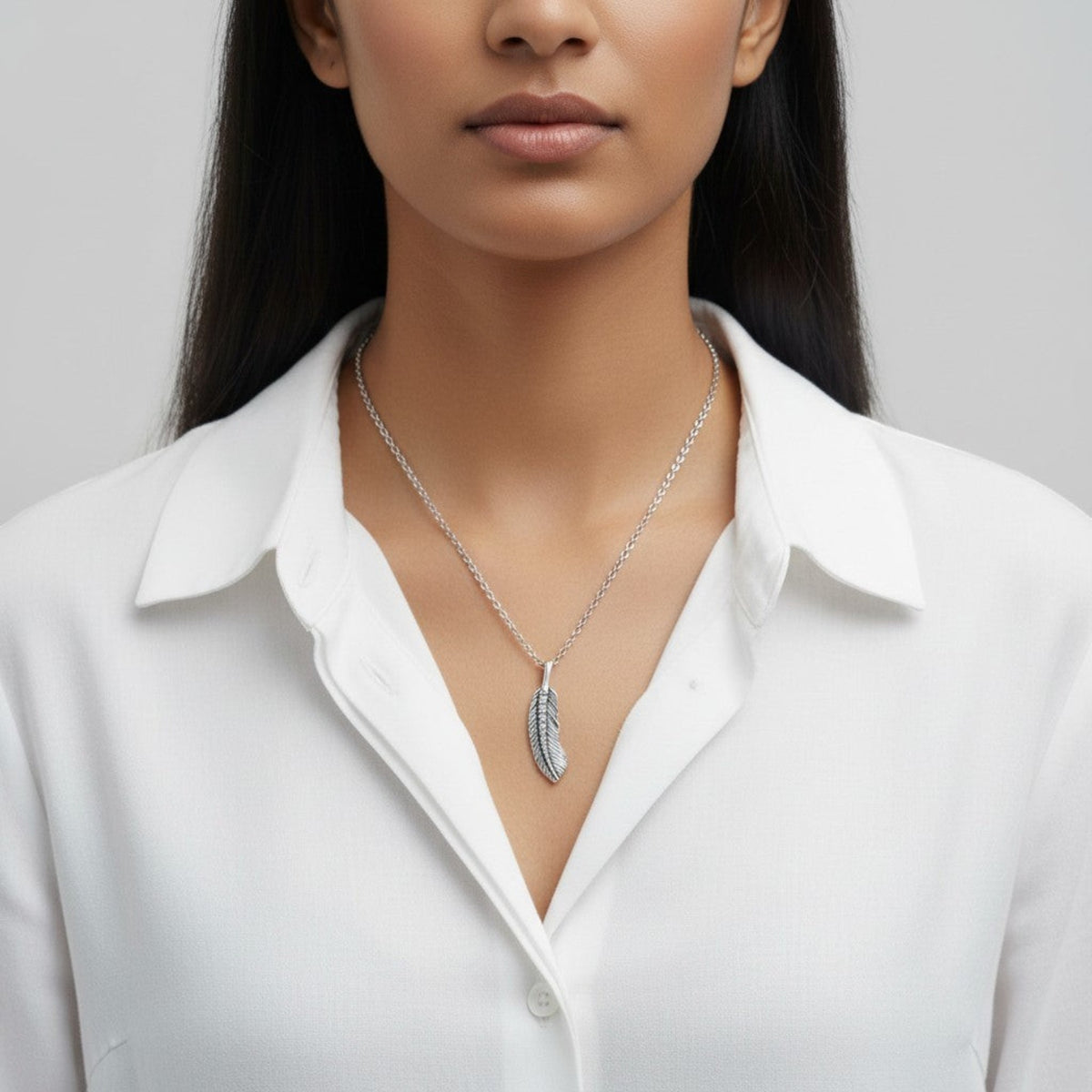 Truelements Jewelry small silver 925 feather pendant with clear zirconia worn by a woman in a white shirt